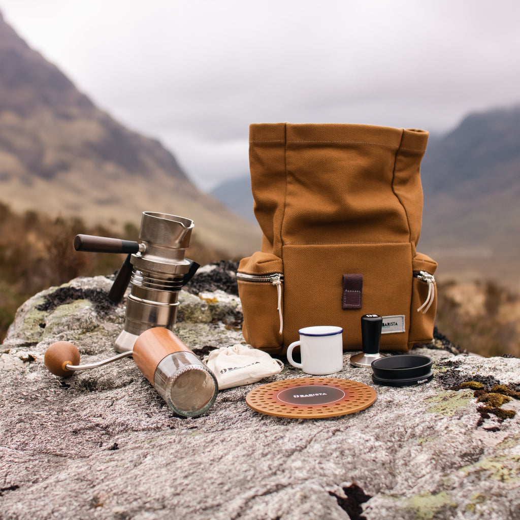 Brown leather bag with camping gear on a rocky outcrop with mountains in the background