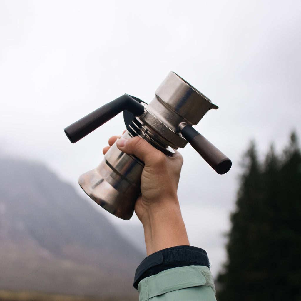 Hand holding a coffee maker against a blurred natural background
